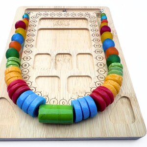 A bamboo bead board with a necklace of colourful recycled glass beads sitting on it. The necklace contains a rainbow of beads in various shapes and sizes, including red, blue, green, orange, and yellow.