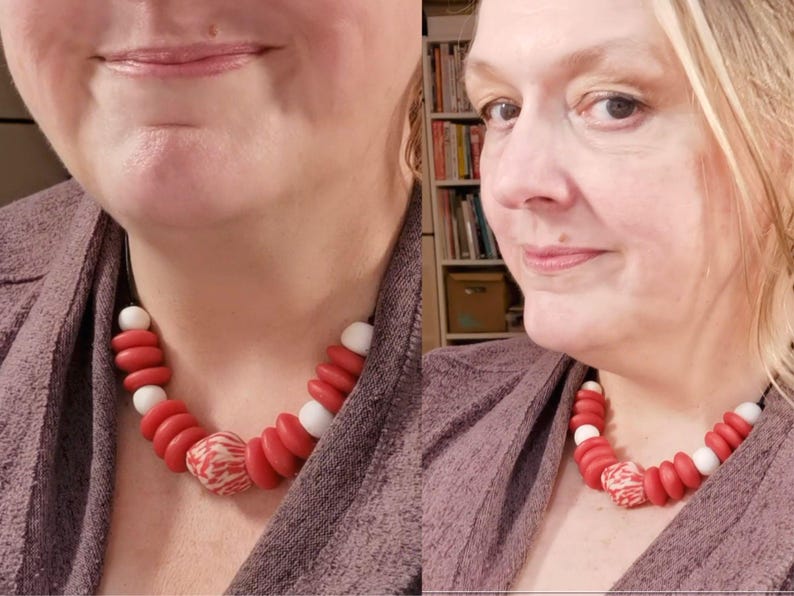 A necklace with red, white, and patterned beads. The necklace is worn around the neck. The beads are a mix of round and disc shapes, creating a bold, colourful statement piece. The necklace is on a black cord.