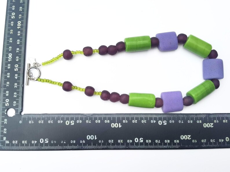 Puede incluir: Collar hecho a mano con cierre plateado. Cuenta con cuentas cil&iacute;ndricas verdes, cuentas cuadradas moradas y cuentas redondas moradas oscuras. El collar mide aproximadamente 46 cm de largo.