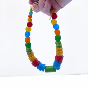 A vibrant necklace featuring a mix of round and cylindrical recycled glass beads in a rainbow of colours. The necklace is held up against a white backdrop.