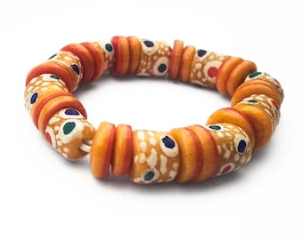 May include: A circular bracelet composed of alternating orange disc-shaped beads and cylindrical tan beads. The cylindrical beads feature a speckled texture with small, circular blue and red painted accents arranged in a repeating pattern.