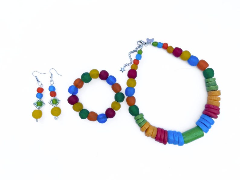 A vibrant jewellery set comprising a necklace, bracelet, and earrings laid out next to each other on a white background. The necklace, bracelet and earrings are all made of a rainbows colours including green, blue, yellow, green and orange. The findings are silver plated and the bracelet is elasticated.