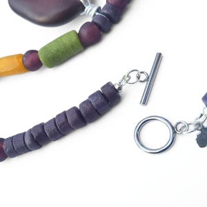 Peut inclure: Gros plan sur un collier fait &agrave; la main avec des perles color&eacute;es. Le collier comprend des perles violettes, vertes et jaunes, un fermoir argent&eacute; et un charm en forme de continent africain.