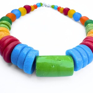 A vibrant chunky choker necklace made with a rainbow of coloured beads. The necklace features a large green centre bead, disc beads in red, orange, yellow, green, and blue and then smaller spherical beads. It is fastened with a silver clasp, creating a striking piece of jewellery.