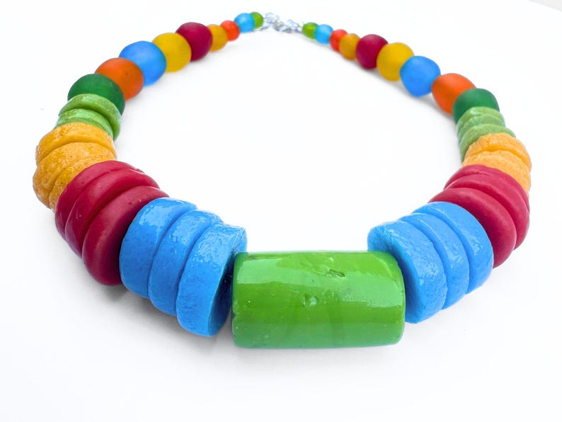 A vibrant chunky choker necklace made with a rainbow of coloured beads. The necklace features a large green centre bead, disc beads in red, orange, yellow, green, and blue and then smaller spherical beads. It is fastened with a silver clasp, creating a striking piece of jewellery.