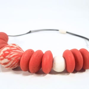 A necklace with coral and white beads on a black cord. The beads are various shapes, including round, oval, and patterned. The background is plain white. The necklace is a piece of jewellery.