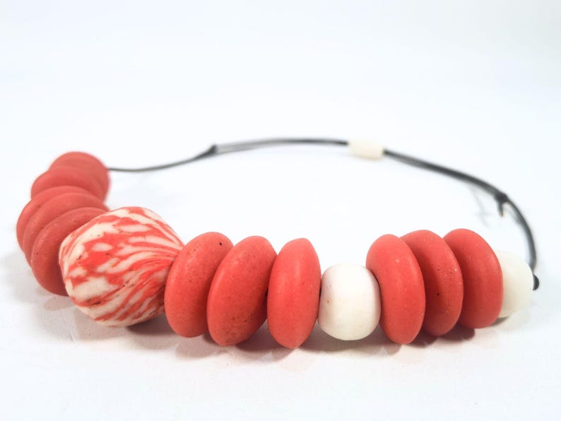 A necklace with coral and white beads on a black cord. The beads are various shapes, including round, oval, and patterned. The background is plain white. The necklace is a piece of jewellery.