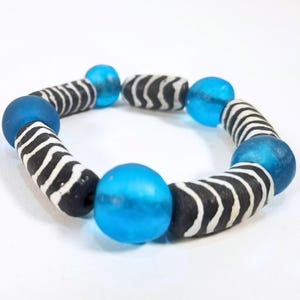 May include: A beaded bracelet featuring alternating blue and black and white striped beads. The bracelet has a circular shape and is made of glass beads. The blue beads are round and the striped beads are cylindrical.