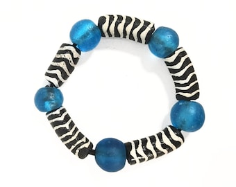May include: A bracelet featuring alternating round translucent blue glass beads and cylindrical black beads with white wavy line patterns. The beads are strung together in a circular arrangement, creating a repeating sequence of blue and patterned black.