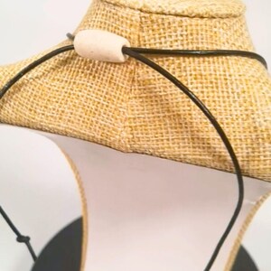 A black necklace with a light-coloured wooden bead clasp. The necklace is displayed on a burlap-covered bust. The cord is made from vegan leather. The bust is on a white surface.