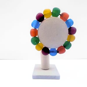 A vibrant beaded bracelet featuring a spectrum of recycled glass round beads, including red, orange, yellow, green, blue, and purple. The bracelet is displayed on a white, round jewellery stand with a square base.