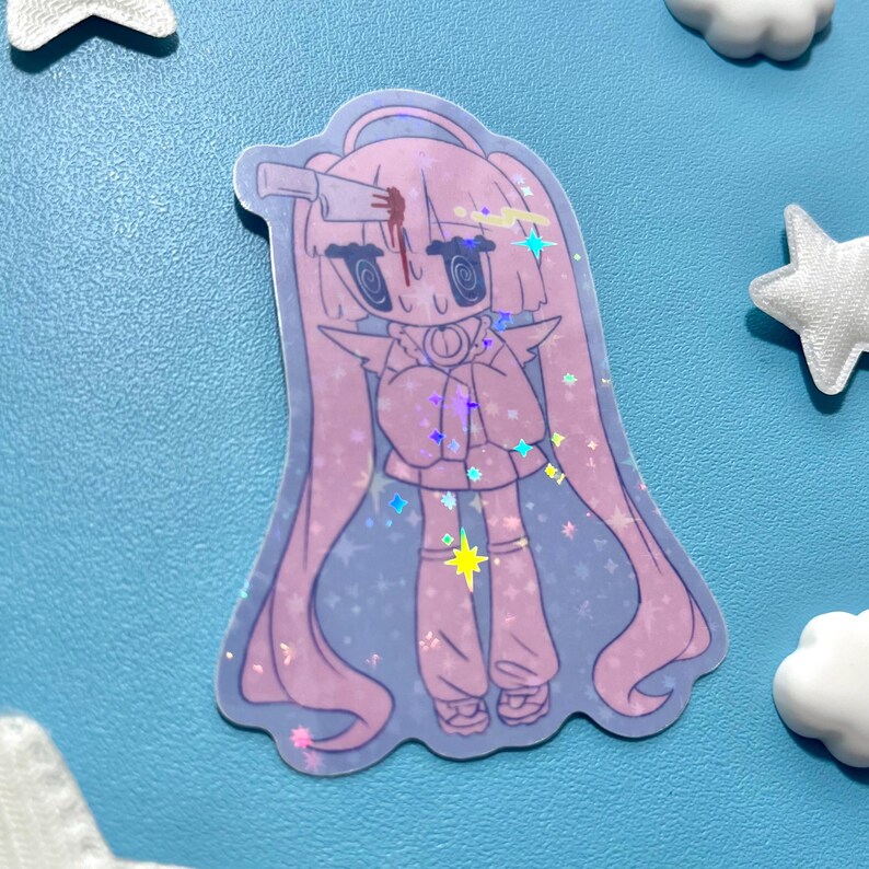 May include: A holographic sticker featuring a cartoon character with long pink hair, a knife in their head, and a blood stain. The character is wearing a pink outfit and has a star-shaped highlight. The sticker is surrounded by star and cloud-shaped decorations.