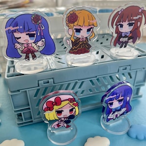 Könnte beinhalten: Eine Sammlung von Anime-Charakter-Standees aus Acryl. Jedes Standee zeigt eine Chibi-Illustration eines weiblichen Charakters mit einzigartigen Frisuren und Outfits. Die Standees werden auf einer hellblauen Plastikkiste präsentiert.
