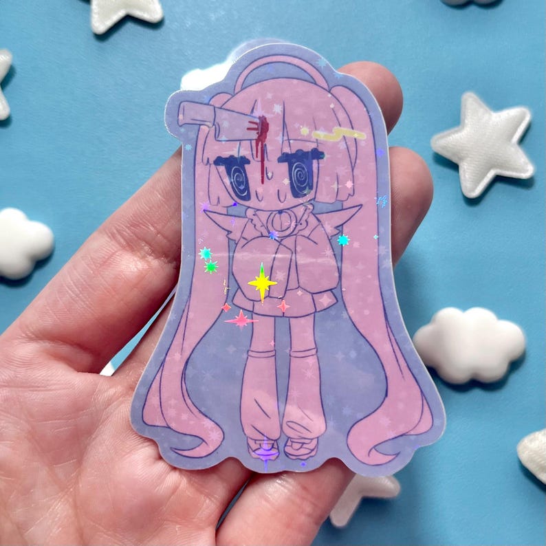 May include: A holographic sticker featuring a cartoon character with long pink hair and a knife in their head. The character has large eyes and is wearing a pink outfit. The sticker has a light blue background with star and cloud-shaped decorations.