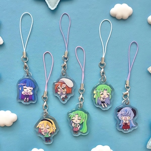 May include: A collection of six anime-style character charms. Each charm features a different character with unique hair and clothing, attached to a silver clasp and a colored lanyard. The background is a light blue.