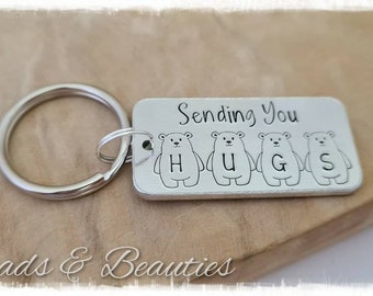 May include: Silver keychain with a rectangular tag that says "Sending You Hugs" with four small polar bear illustrations spelling out the word "HUGS".