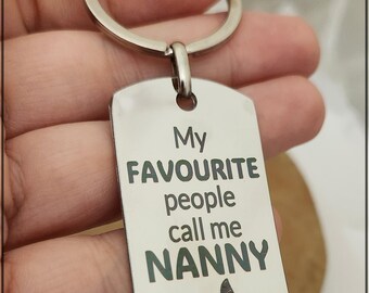 May include: A silver-colored rectangular keychain with a key ring. The keychain has the text "My FAVOURITE people call me NANNY" in dark green, with a butterfly graphic at the bottom. A thoughtful gift for a nanny.