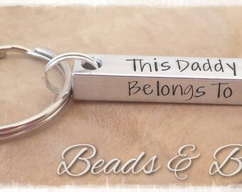 May include: Silver keychain with a rectangular bar that reads "This Daddy Belongs To".