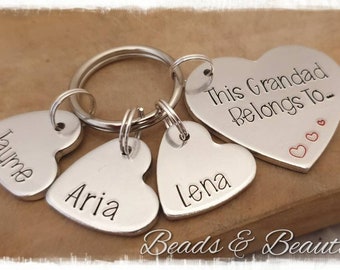 May include: Silver heart-shaped keychain with the inscription "This Grandad Belongs To-" and three smaller heart-shaped tags with the names "Jayme", "Aria", and "Lena".