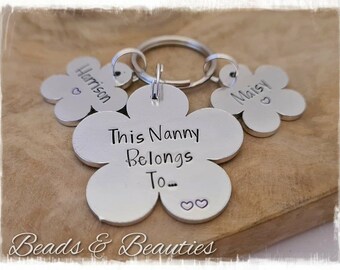 May include: Silver flower-shaped keychain with the text "This Nanny Belongs To..." and two smaller flower-shaped tags with the names "Harrison" and "Maisie".