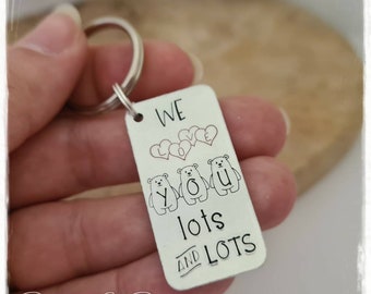 May include: Silver keychain with a rectangular tag that reads "WE LOVE YOU lots and lots". The tag features three small bears holding the letters "YOU" and two hearts above the bears.