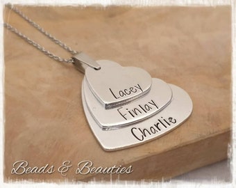 May include: Silver necklace with three layered heart pendants. The hearts are engraved with the names Lacey, Finlay, and Charlie.