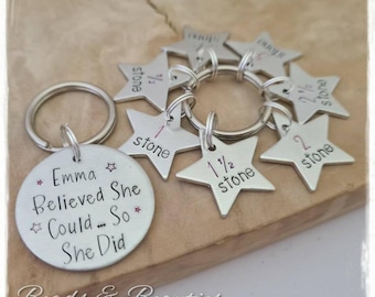 May include: A silver keychain with a round charm that reads "Emma Believed She Could... So She Did" and several star-shaped charms with the words "1 stone", "1 1/2 stone", "2 stone" and "2 1/2 stone" inscribed on them.