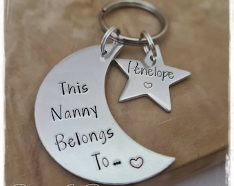 May include: Silver crescent moon keychain with the text "This Nanny Belongs To" and a small heart. A silver star charm with the name "Penelope" and a small heart is attached to the keychain.