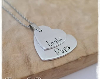 May include: Silver necklace with two layered heart pendants. The top heart is engraved with the name "Layla" and the bottom heart is engraved with the name "Pops".