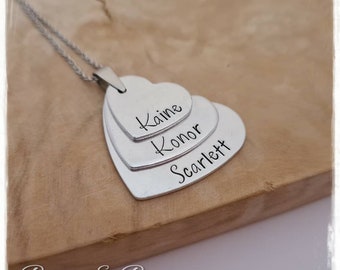 May include: Silver necklace with three layered heart charms. The hearts are engraved with the names Kaine, Konor, and Scarlett.