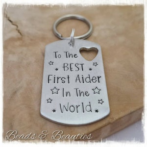 May include: Silver keyring with a heart cutout and the text "To The ☆ BEST ☆ First Aider ☆ In The ☆ World ☆".