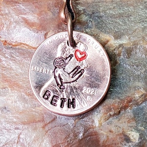 May include: A copper penny keychain with a small sloth holding a red heart. The penny has the words "In God We Trust" and "Liberty" on it. The year 2021 is engraved on the penny. The word "Beth" is engraved on the bottom of the penny.