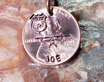 Op de afbeelding: Een koperen sleutelhanger met een penny waarop een politiebadge, een helikopter en het woord "JOE" gegraveerd zijn. De sleutelhanger is bevestigd aan een koperen sleutelring.