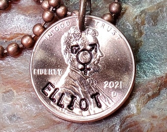 May include: A copper penny necklace with a ball chain. The penny has been customized with the name "Elliot" and a transgender symbol. The year 2021 is also engraved on the penny.