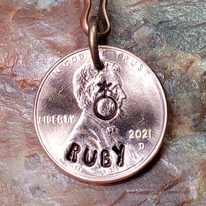 May include: A copper penny keychain with the words "In God We Trust" and "Liberty" engraved on it. The year 2021 is also engraved on the penny. The word "Ruby" is engraved on the bottom of the penny.
