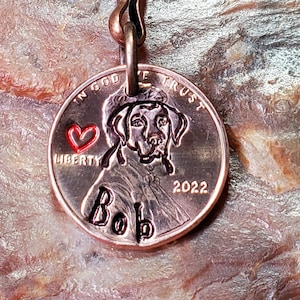 May include: A copper penny keychain with a personalized image of a dog and the name "Bob" engraved on it. The penny has the words "In God We Trust" and "Liberty" on it, along with the year 2022.