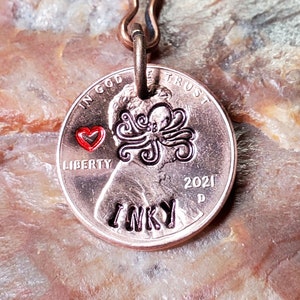 May include: A copper-colored key chain with a 2021 US penny attached. The penny has an octopus design and the word "INKY" engraved on it. A red heart is engraved next to the octopus.