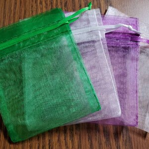 Puede incluir: Cuatro peque&ntilde;as bolsas de organza en verde, blanco, morado y blanco. Las bolsas est&aacute;n hechas de tela transparente y tienen un cierre de cord&oacute;n.