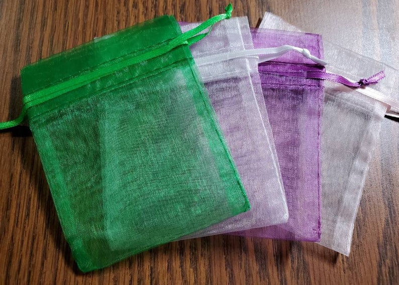 Puede incluir: Cuatro peque&ntilde;as bolsas de organza en verde, blanco, morado y blanco. Las bolsas est&aacute;n hechas de tela transparente y tienen un cierre de cord&oacute;n.