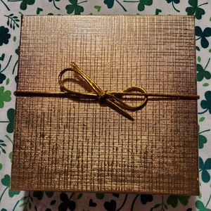 Op de afbeelding: Een gouden geschenkdoos met een gouden lint gebonden in een strik.