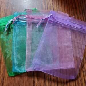 May include: Four sheer organza gift bags in different colors: green, blue, pink, and purple. The bags are made of a delicate, translucent fabric and have a drawstring closure.