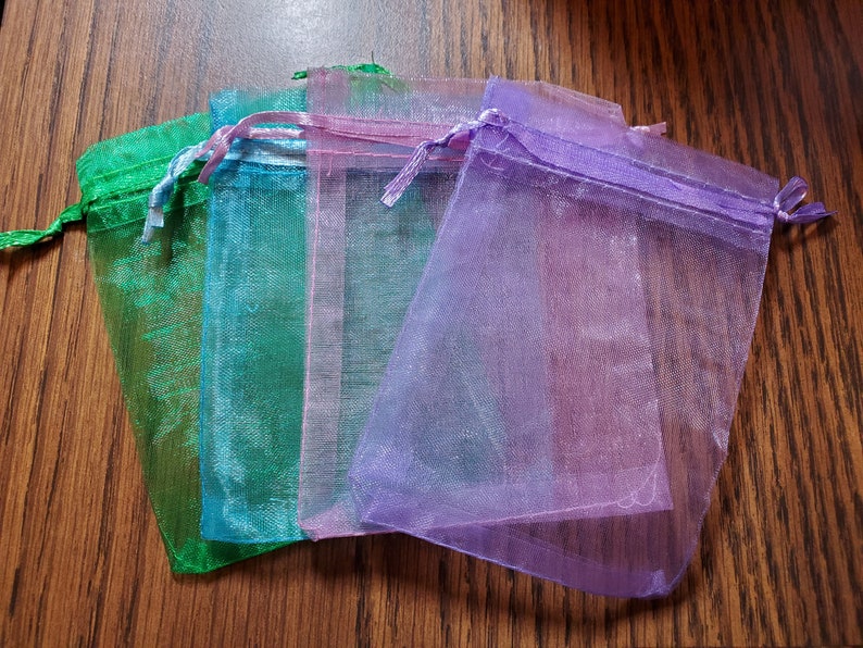May include: Four sheer organza gift bags in different colors: green, blue, pink, and purple. The bags are made of a delicate, translucent fabric and have a drawstring closure.