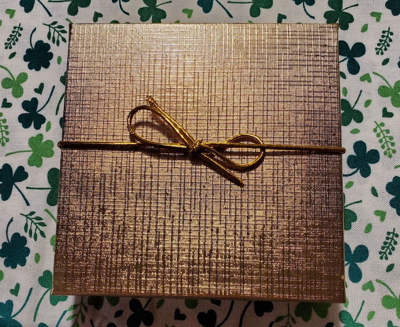 Puede incluir: Una caja de regalo dorada con una cinta dorada atada en un lazo.