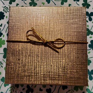 May include: A gold gift box with a gold ribbon tied in a bow.