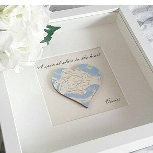 May include: A white frame with a white mat and a heart-shaped map of Venice inside. The map is on a wooden base and the text "A special place in the heart" is written above the map. The text "Venice" is written below the map.