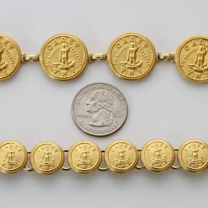 May include: A gold chain necklace with a series of round gold medallions. Each medallion features a raised image of a person standing on a ship's anchor with the text "CLUBBER" and "V.M.I." around the image.