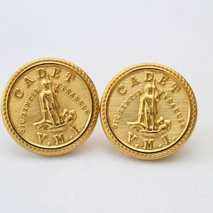 May include: Two gold-colored metal buttons with a raised design. The buttons feature a figure standing on a boat with the text "CADET" and "SIG. STVDIORVM. ACADEMIAE NAVALIS" around the figure. The text "V.M." is at the bottom of the button.