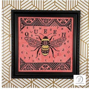 May include: Cross-stitch pattern with a pink background and black stitching. The pattern features a bee with yellow and black stripes and the word "QUEEN" surrounding the bee. The letters are arranged in a circle around the bee.