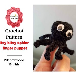 Puede incluir: Una marioneta de araña de crochet negro con grandes ojos saltones blancos. La marioneta está en un dedo y el fondo es una pared gris claro. El texto "Itsy bitsy spider finger puppet" está escrito en letras rojas sobre un fondo blanco.