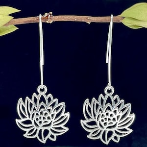 May include: A pair of silver dangle earrings featuring a delicate lotus flower design. The earrings are made of metal and have a simple, elegant style.